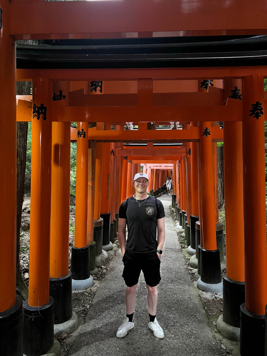 Alexander Ingare standing in a tunnel of vermilion torii gates on a forest path