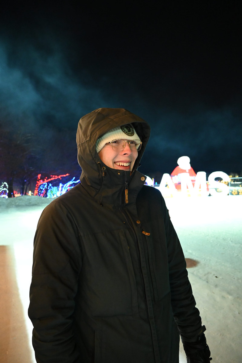 Alexander Ingare in a hooded winter coat at night, standing on packed snow in
                    front of an illuminated display
